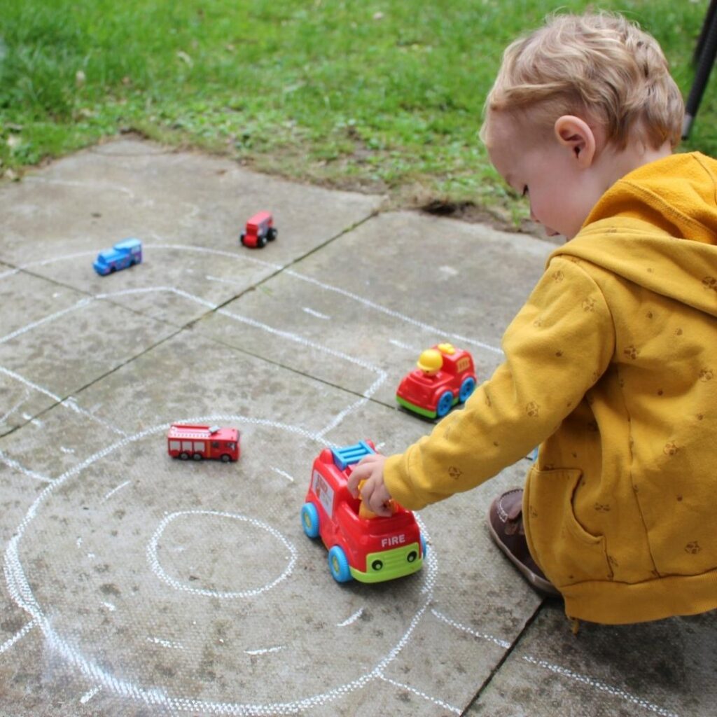Toddler playing with car on roads drawn with chalk on the sidewalk