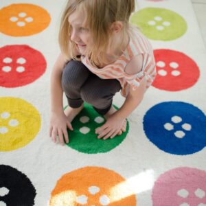 girl squatting on a rug with colorful dots.