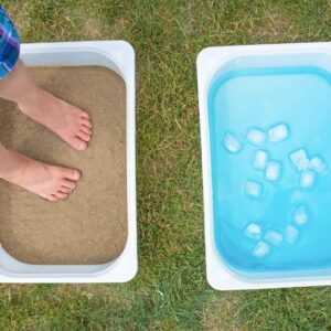 child standing in a box of sand. Also shows a box of ice water for animal habitat sensory walk