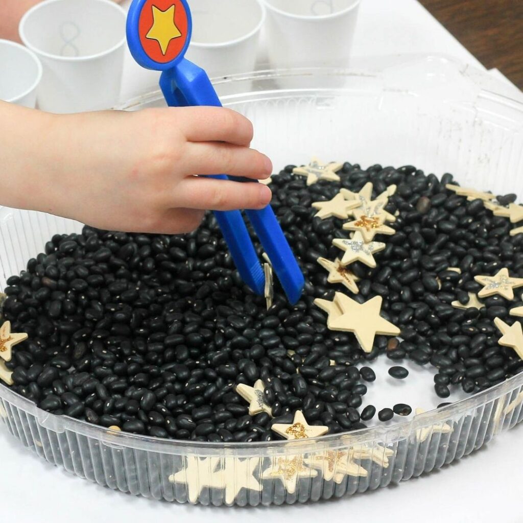Space theme preschool sensory bin made with black beans and stars.